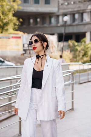 Stylish Young Woman in Striped Suit with Sunglasses Posing Outdoors.の写真素材