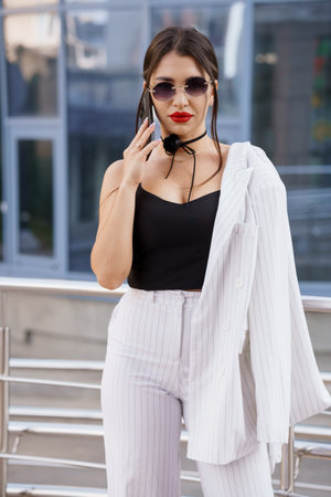 Stylish Woman in Pinstripe Suit With Sunglasses and Bold Red Lips Posing Confidently Outdoors.の写真素材