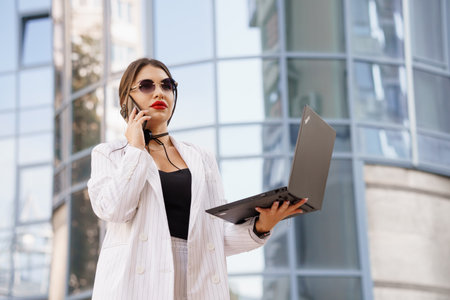 Stylish Businesswoman with Laptop and Headset in Urban Environment.