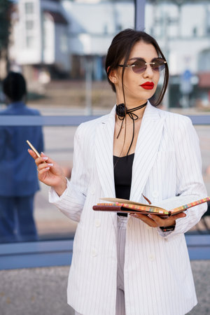 Stylish Woman in Chic Striped Blazer with Notebook and Sunglasses.の写真素材