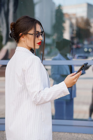 Stylish Businesswoman in Pinstripe Suit Engaging with Smartphone in Urban Setting.の写真素材