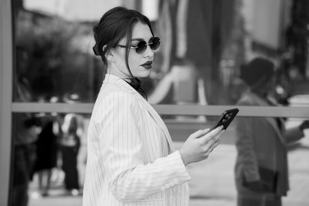 Chic Elegance: A Stylish Woman in a Pinstripe Suit and Sunglasses Holding a Smartphone.の写真素材