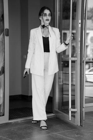 Chic Businesswoman Exiting Modern Office in Striped Suit and Sunglasses.の写真素材