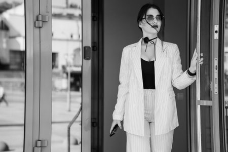 Elegant Woman in Striped Suit Emerging from Modern Glass Doors.の写真素材