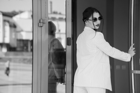 Chic Businesswoman Posing Elegantly by the Glass Door in Black and White.の写真素材