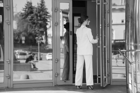 Elegant Businesswoman Exiting Modern Glass Building in Stylish Pinstripe Suit.の写真素材