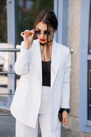 Chic Businesswoman in Pinstripe Suit with Sunglasses Posing Outdoors.