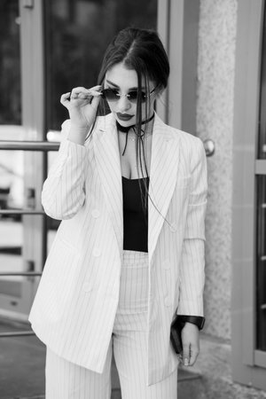 Stylish woman in a pinstripe suit with sunglasses exuding confidence and elegance in urban setting.の写真素材