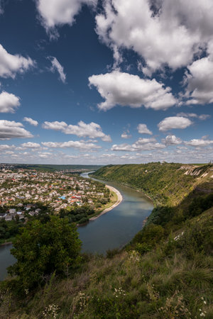 Serene Aerial View of a Winding River Surrounded by Lush Green Hills and a Quaint Town Under a Cloudy Sky.の写真素材