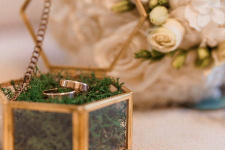 Elegant Wedding Rings in a Glass Box Surrounded by Flowers.