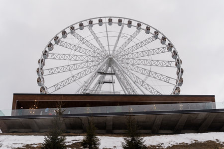 Modern Ferris Wheel Against a Gray Sky Overlooking a Snowy Landscape.の写真素材