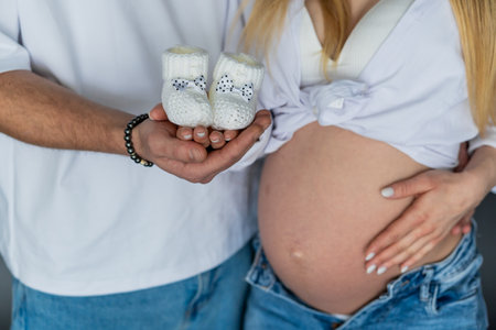 Expecting Parents Holding Baby Booties with Pregnant Belly in Focus.の写真素材