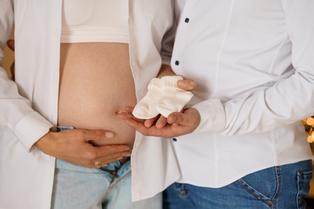 Expecting Parents Holding Baby Socks with Pregnant Belly in Focus.の写真素材