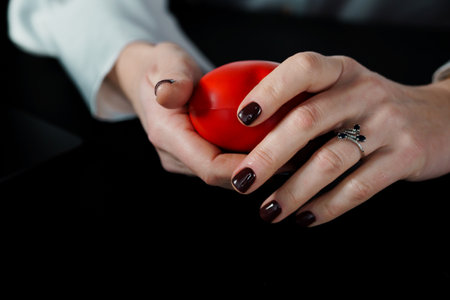 Close-up of Hands Holding a Red Stress Ball with Dark Nail Polish.