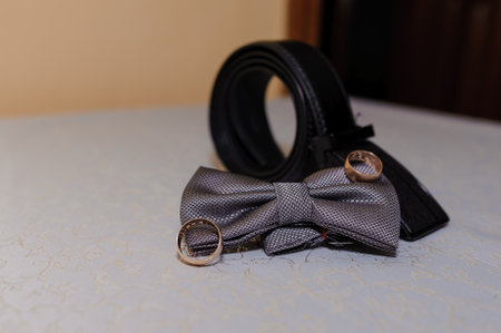 Elegant Accessories for a Special Occasion Featuring a Gray Bow Tie, Wedding Rings, and a Leather Belt.の写真素材