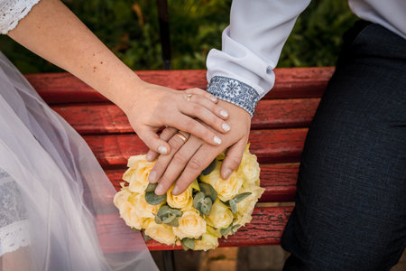 A Romantic Moment: Hands Intertwined with a Bridal Bouquet on a Rustic Bench.の写真素材