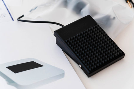 Close-Up View of Black Foot Pedal Switch on Desk with Electronic Device and Cables.