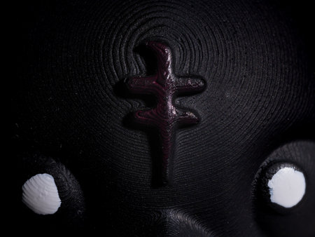 Close-Up Artistic Dark Abstract Textured Sculpture with White Eyes and Central Raised Symbol.の写真素材