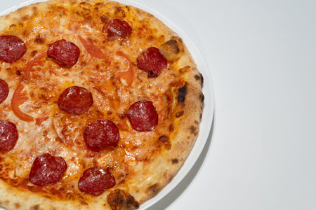 Freshly Baked Pepperoni Pizza on White Ceramic Plate With Melted Cheese and Tomato Slices in...