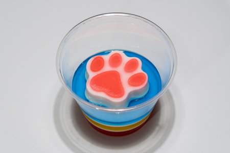 Colorful Layered Dessert Jelly Cup with Paw Shaped Topper on White Background.