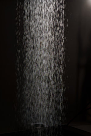 Cascading Water Droplets Illuminated in Dark Background Creating Abstract Rainfall Effect Photography.の写真素材
