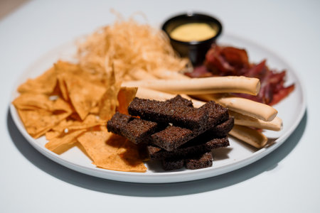Variety snack plate with tortilla chips, dried meat, breadsticks and creamy dip on white background.の写真素材