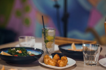 Delicious restaurant meal with fresh salad, fried snacks and refreshing drinks on wooden table with colorful background.の写真素材