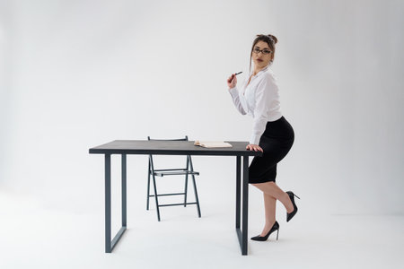 Attractive businesswoman leaning on table with paper document, thoughtful pose.の写真素材