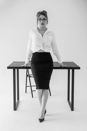 Elegant businesswoman posing at office table in black and white portrait.の写真素材