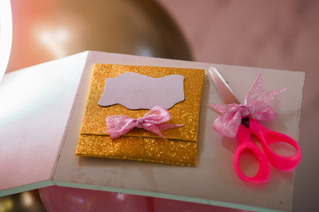 A charming miniature crafting scene featuring a golden glittery card with a pink bow and small pink...