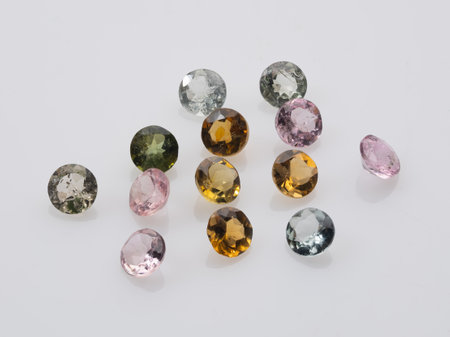 Assortment of vibrant, faceted natural tourmaline gemstones in a range of colors, including pink, yellow, orange, green, and blue, scattered on a white background.の写真素材