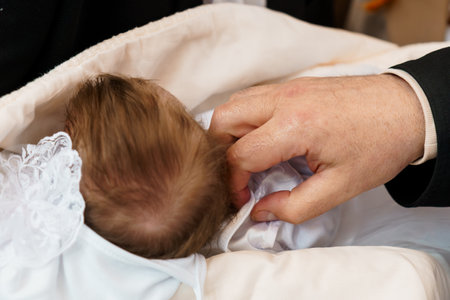A tender moment during a baby's baptism ceremony, showing a priest's hands gently touching the head...