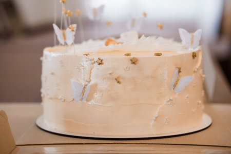 A beautifully decorated light peach frosted cake adorned with delicate white butterflies and golden stars, set on a wooden surface, creating a whimsical and elegant dessert presentation.の写真素材