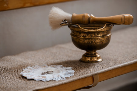 A vintage brass cup holds wedding rings resting on a lace doily next to a polishing brush on a...