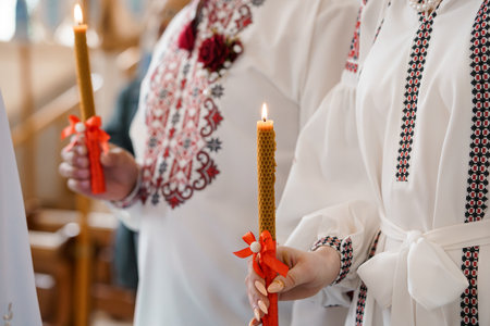 Close-up of hands holding lit beeswax candles during a traditional Ukrainian Orthodox wedding...