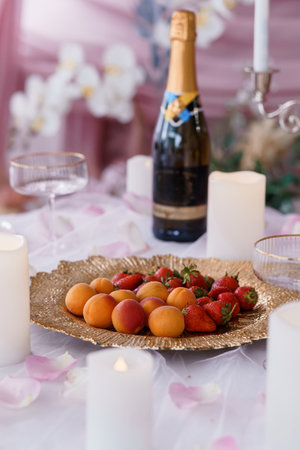 A lavish table arrangement features champagne, fresh strawberries, peaches, and lit candles, enveloped in a romantic pink aesthetic, ideal for celebrating weddings or special occasionsの写真素材