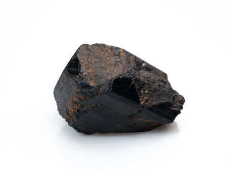 A close-up shot of a roughly cut black tourmaline crystal with metallic flecks, showing its natural form against a clean white backdropの写真素材