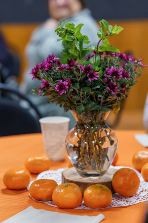 A warm, inviting still life featuring a glass vase brimming with vibrant purple chrysanthemums and fresh mint, surrounded by juicy oranges on a festive orange table settingの写真素材