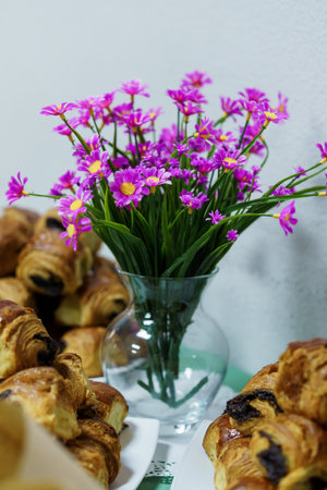 A beautiful still life arrangement featuring a glass vase filled with vibrant purple cosmos flowers beside a plate of freshly baked golden croissants, evoking a peaceful morning breakfast vibeの写真素材