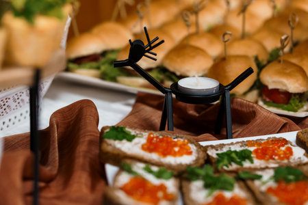 Close-up shot of a festive party buffet featuring reindeer-shaped candle holders alongside delicate caviar canapes and miniature burgers, creating an inviting holiday atmosphereの写真素材