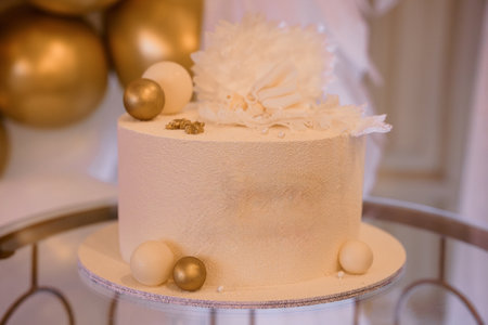 A sophisticated tiered wedding cake adorned with a delicate white floral arrangement and shimmering...
