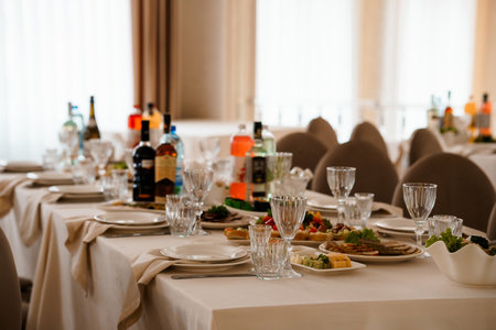 A beautifully arranged wedding reception table features fine china, silverware, wine glasses, and appetizers. a beige and cream color palette creates a warm, formal atmosphereの写真素材