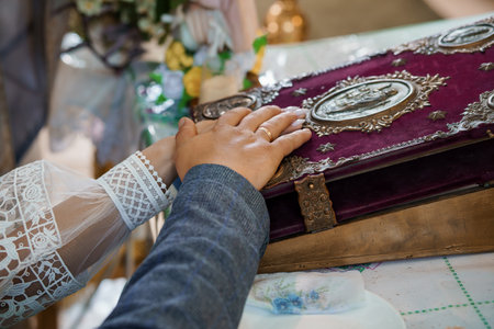 Wedding Ceremony Hands Over Holy Book: Marriage Vows, Church Interior, Silver Rings, Lace, Burgundy Velvet, Religious Ritual, Close-Up View.の写真素材