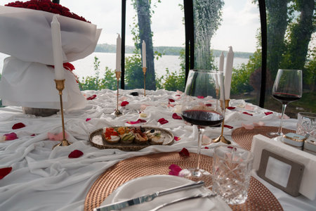 Intimate dining setup with a bouquet of red roses, wine glasses, lit candles, and a cheese platter...