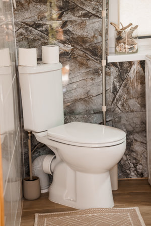A clean, contemporary bathroom features a white toilet against a striking marble wall, with subtle wooden accents and a neutral color palette, showcasing interior designの写真素材