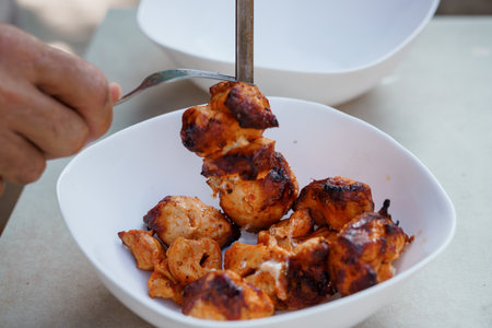 A close-up shot showcases succulent grilled chicken skewers being served onto white plates, presenting a mouthwatering culinary scene perfect for food blogs and menusの写真素材