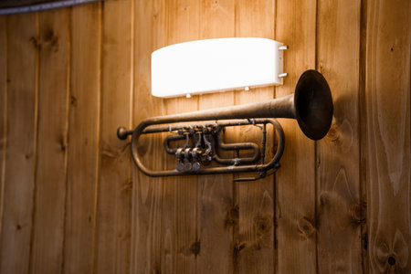 Artistic wall light fixture ingeniously repurposed from a vintage brass trumpet, attached to rustic...