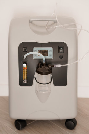 A white portable oxygen concentrator sits indoors with its water chamber visible, providing supplemental oxygen for respiratory support and health managementの写真素材