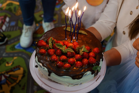 A beautifully decorated chocolate cake adorned with fresh strawberries and lit candles is the centerpiece of a birthday party, suggesting joy, celebration, and sweet indulgenceの写真素材