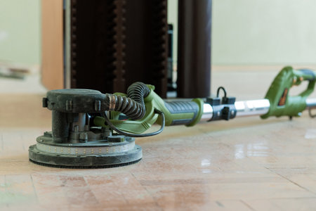 A green drywall sander and its extraction hose are laid on polished marble tile flooring during a home renovation project, showing interior floor careの写真素材